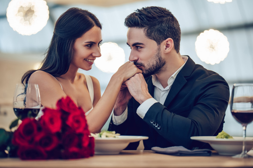 Glückliches Paar beim Date im Restaurant mit Rotwein und Rosen.