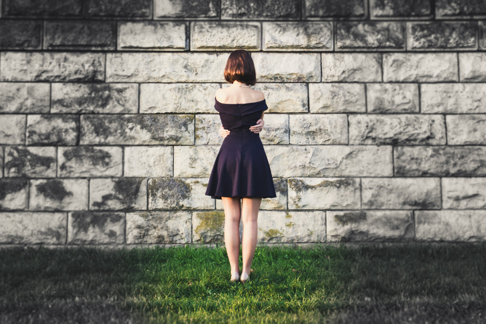 Unsichere Frau steht in gepunktetem Kleid vor einer Mauer.